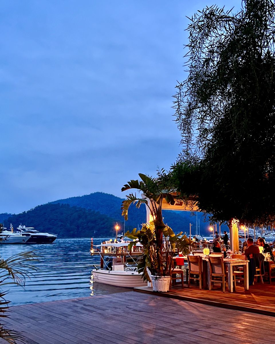 Akşam Göcek Marina: su kenarında restoran masaları ve demirli tekneler